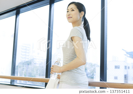 一名女子站在窗邊，手裡拿著一個塑膠瓶 137351411