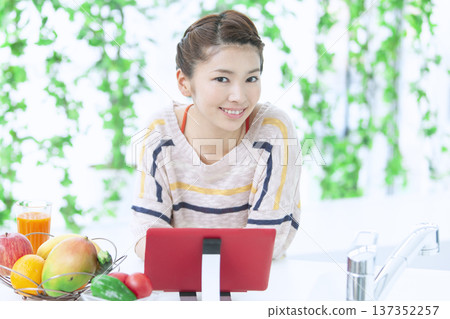 A woman who manipulates a tablet in the kitchen A woman who manipulates a tablet in the kitchen 137352257