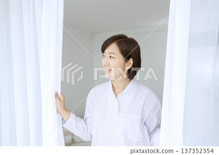 一位穿著睡衣的中年婦女正在拉開窗簾。 137352354