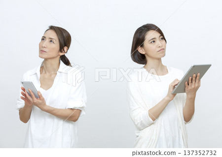 Mother and daughter operating a tablet and smartphone 137352732