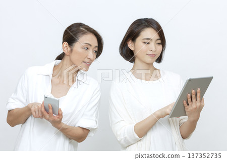 Mother and daughter operating a tablet and smartphone Mother and daughter operating a tablet and smartphone 137352735