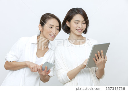 Mother and daughter operating a tablet and smartphone Mother and daughter operating a tablet and smartphone 137352736