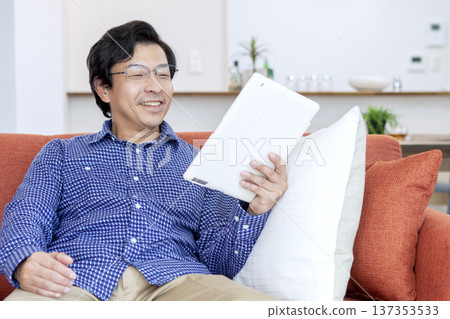 Man looking at tablet on sofa Man looking at tablet on sofa 137353533
