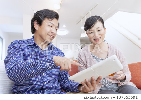 一對夫婦一邊看著平板電腦一邊聊天。 137353591