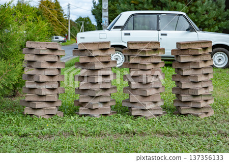 Four stacks of interlocking paving stones on grass, near a white car Four stacks of interlocking paving stones on grass, near a white car 137356133