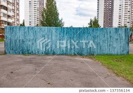 Weathered teal wooden fence against urban high-rise buildings and cloudy sky 137356134