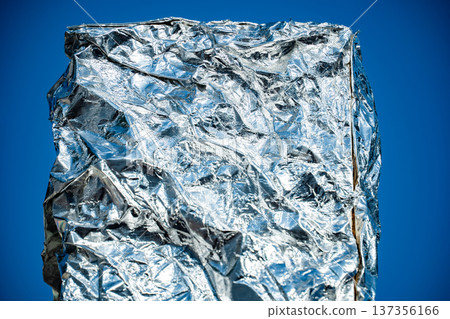 Crumpled aluminum foil surface texture shimmering in sunlight against blue background 137356166