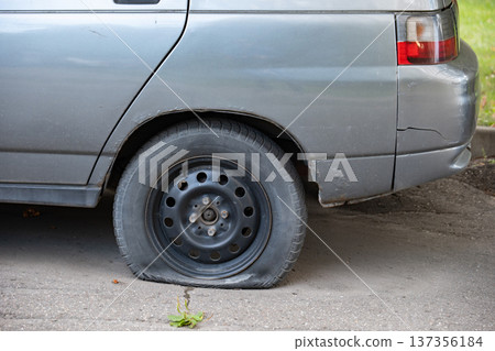 Old gray car with a flat, deflated rear tire on asphalt, needing repair Old gray car with a flat, deflated rear tire on asphalt, needing repair 137356184