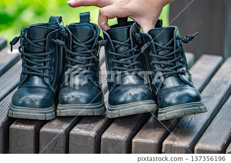 Child's scuffed black boots lined up on a wooden bench, symbolizing active childhood Child's scuffed black boots lined up on a wooden bench, symbolizing active childhood 137356196