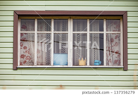 Green house wall featuring a window with patterned curtains and small objects 137356279