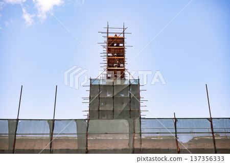 Building renovation with scaffolding and safety netting during construction process 137356333