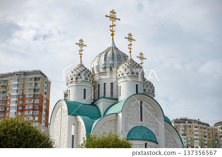 Russian Orthodox Church domes with crosses standing against cloudy sky and urban buildings 137356567