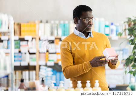 Middle-aged man reading label on box of medicine in drugstore Middle-aged man reading label on box of medicine in drugstore 137356733