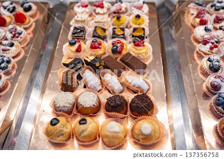 Displaying a variety of delicious mini pastries, cakes, and fruit tarts on silver trays Displaying a variety of delicious mini pastries, cakes, and fruit tarts on silver trays 137356758