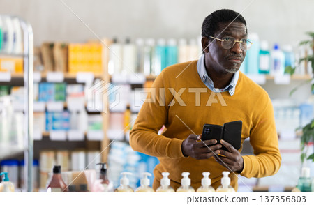 Middle-aged man checking list of medications on phone in drugstore Middle-aged man checking list of medications on phone in drugstore 137356803