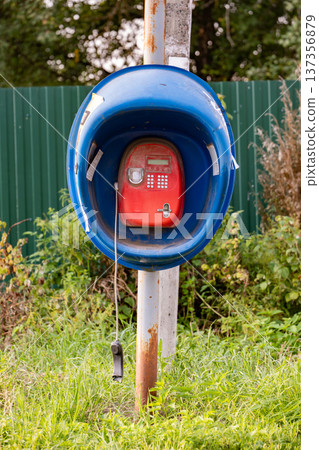 Abandoned classic blue and red payphone on a street with green grass 137356879