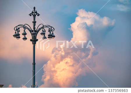 Vintage street lamp standing against a dramatic evening sky with warm sunset clouds Vintage street lamp standing against a dramatic evening sky with warm sunset clouds 137356983