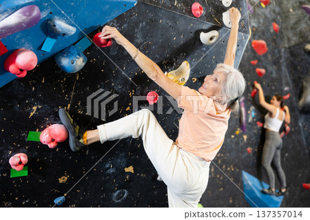 Determined senior woman doing her best at climbing artificial wall Determined senior woman doing her best at climbing artificial wall 137357014