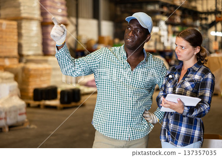 Man talking with young woman in warehouse and pointing with his hand at boxes of products 137357035