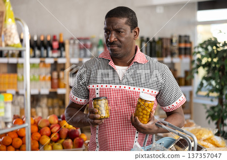 African man make choice choose consider canned pickled olives in store 137357047