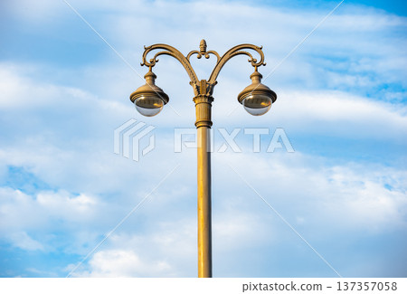 Vintage street lamp with ornate design against a bright blue sky with clouds Vintage street lamp with ornate design against a bright blue sky with clouds 137357058