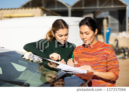 Focused female farmers signing papers near car at farm Focused female farmers signing papers near car at farm 137357066