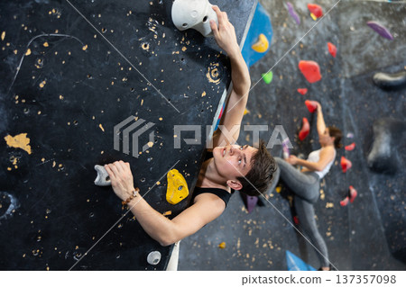 young muscular male sportsman climbing black wall for bouldering in gym young muscular male sportsman climbing black wall for bouldering in gym 137357098
