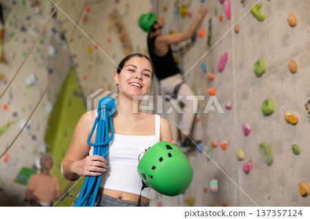 Happy sporty young female holding helmet and blue ropes while standing against concrete wall background. Rock, mountain, industrial albinism climbing concept 137357124