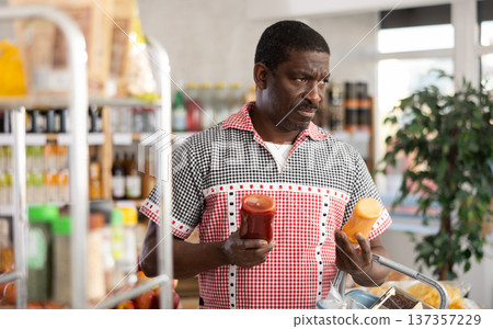 African man buyer select choose thoughtfully at bottles of different sauces African man buyer select choose thoughtfully at bottles of different sauces 137357229