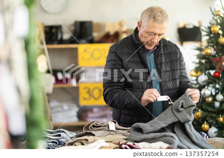 Mature male shopper selects sweater in fashionable clothing boutique 137357254