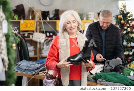 Mature woman standing on the background of a Christmas tree and choosing platform boots Mature woman standing on the background of a Christmas tree and choosing platform boots 137357260