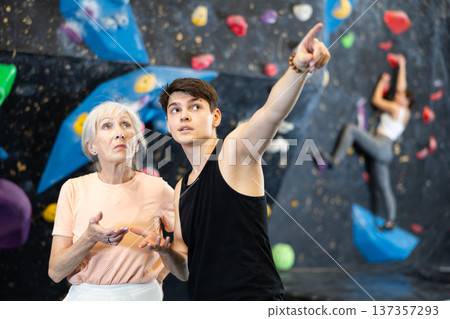 coach shows beginner female athlete simple routes for climbing on artificial dark bouldering wall coach shows beginner female athlete simple routes for climbing on artificial dark bouldering wall 137357293