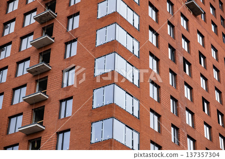 Modern building facade featuring red brick, many windows, and concrete balconies Modern building facade featuring red brick, many windows, and concrete balconies 137357304
