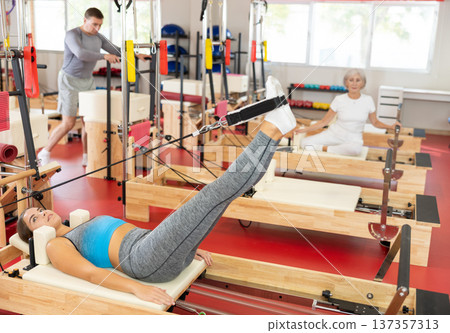 Girl is engaged in Pilates simulator with cable and ropes for stretching leg muscles Girl is engaged in Pilates simulator with cable and ropes for stretching leg muscles 137357313
