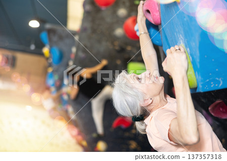 Mature female fitness climber training at bouldering gym.Woman rise up on artificial climbing wall Mature female fitness climber training at bouldering gym.Woman rise up on artificial climbing wall 137357318
