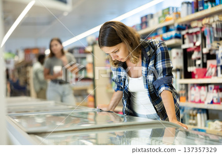 Female shopper carefully chooses frozen food in grocery supermarket Female shopper carefully chooses frozen food in grocery supermarket 137357329