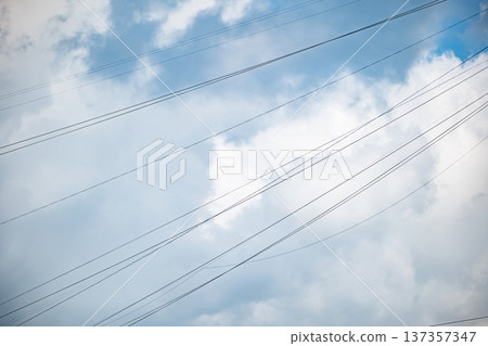 Power lines drawing across cloudy blue sky, representing modern connection and infrastructure Power lines drawing across cloudy blue sky, representing modern connection and infrastructure 137357347