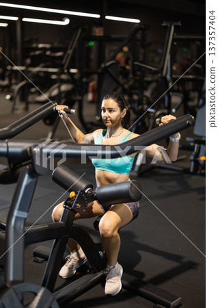 In gym, woman uses lat pulldowm machine to strengthen arm muscles In gym, woman uses lat pulldowm machine to strengthen arm muscles 137357404