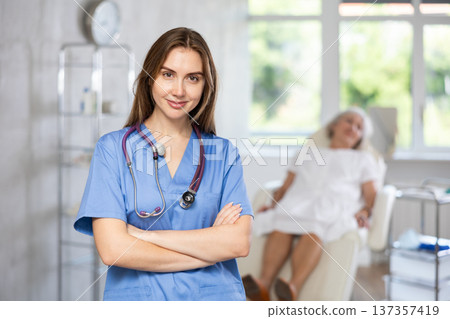 Smiling senior woman doctor in uniform with woman patient lying behind in clinic. 137357419