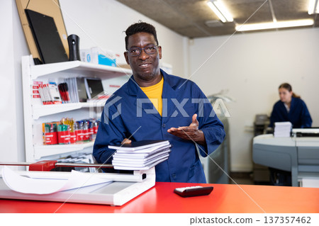 Excited middle-aged African American male typographer in uniform showing notepads in the typography 137357462