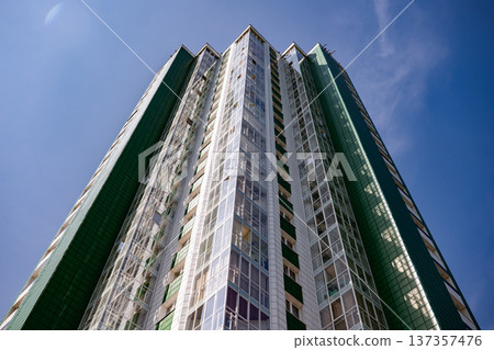 Modern residential tower reaching into blue sky with green and white facade Modern residential tower reaching into blue sky with green and white facade 137357476