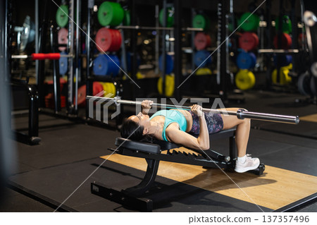 Woman performing bench chest press with barbell in gym Woman performing bench chest press with barbell in gym 137357496
