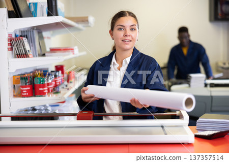 Happy young female specialist in a blue uniform holding whatman in a roll in the typography Happy young female specialist in a blue uniform holding whatman in a roll in the typography 137357514