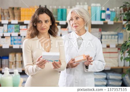 Woman choose antiallergic pills in pharmacy, mature woman pharmacist in background 137357535
