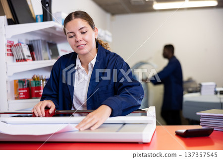 Work in printing house - woman cuts paper with professional cutter 137357545
