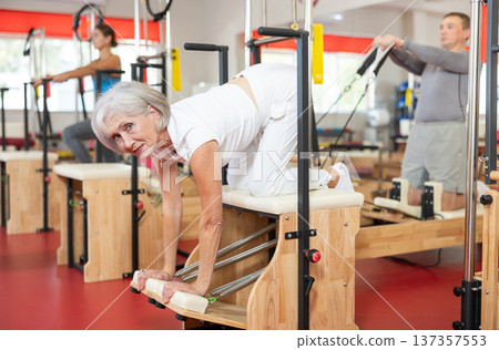 Senior woman does gymnastics in gym and performs bends and stretches on wunda chair Senior woman does gymnastics in gym and performs bends and stretches on wunda chair 137357553