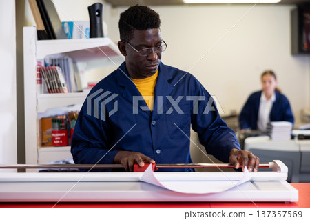 Serious print shop worker cuts paper on professional cutter Serious print shop worker cuts paper on professional cutter 137357569