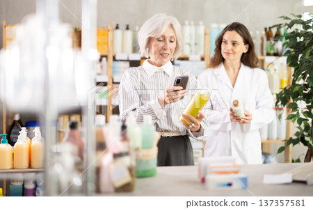 Mature woman in pharmacy scans QR code on shampoo, woman pharmacist in background 137357581
