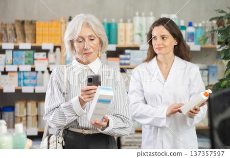 Mature woman in pharmacy scans QR code on cream, woman pharmacist in background 137357597