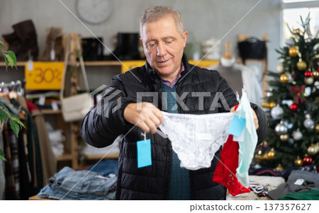 Mature male shopper selects ladies panties as a Christmas gift in fashionable clothing boutique Mature male shopper selects ladies panties as a Christmas gift in fashionable clothing boutique 137357627
